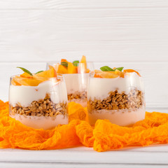 Persimmon creamy trifle in beautiful glasses, fresh ripe fruit slices on white wooden background. Healthy vegetarian food. Delicious dessert. Close up photography. Selective focus.