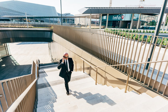 Mature businessman outdoors, walking up steps, using smartphone
