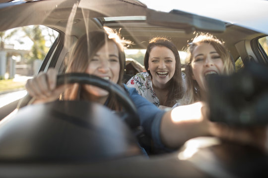 Three young women in car, driver adjusting sat nav on window