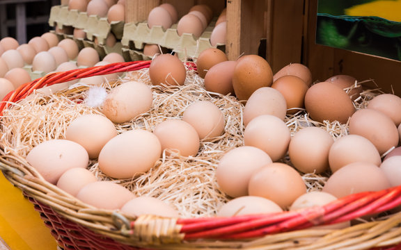 Brown chicken eggs leaning on straw in wooden basket at matket,outdoor.
