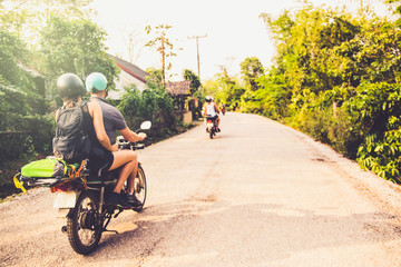 Happy Friends driving motorcycles while driving thought rural area in a tropical place. Travel, adventure and summer concept.