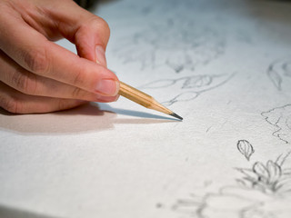 Woman's hand holding a pencil and drawing a flowers on watercolor paper