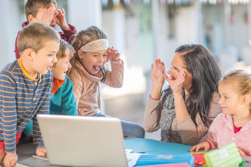 Mid adult woman, sitting with young children, looking at laptop