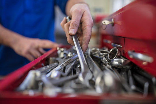 Hands of male car mechanic selecting wrench from tool box  in repair garage