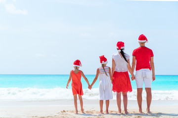 Happy family in red Santa hats on a tropical beach celebrating Christmas vacation