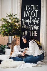 Obraz premium Close-up photo of little girl in knitted sweater kiss her mother while sitting on sofa at Christmas