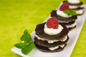 Layers of chocolate biscuits filled with whipped cream and small raspberry pieces and decorated with a sprig of mint and a raspberry on top.