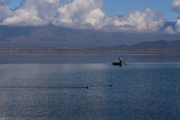 Obraz premium Doiran Lake seen from the town of Stari Doiran, Macedonia. Sunny autumn day, poor fisherman with old fishing boat in the calm lake. Greece on other side of the lake