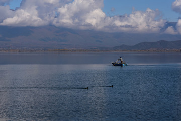 Doiran Lake seen from the town of Stari Doiran, Macedonia. Sunny autumn day, poor fisherman with old fishing boat in the calm lake. Greece on other side of the lake