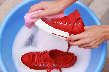 Woman washing sneakers with rag over plastic basin, closeup