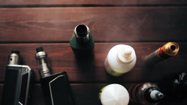 E-cig mods or Electronic cigarettes for vaping on a wooden background. Vape devices and e-liquids in Smoke Cloud of vapour, toned
