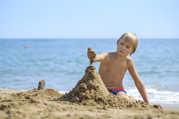 Child playing with sand and building sandy castle 1