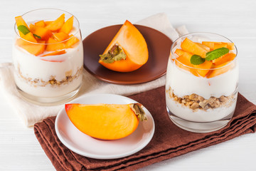 Persimmon creamy trifle in beautiful glasses, fresh ripe fruit slices on white wooden background. Healthy vegetarian food. Delicious dessert. Close up photography. Selective focus.