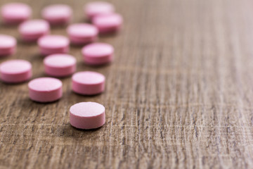 Heap of pink capsules on wooden background.