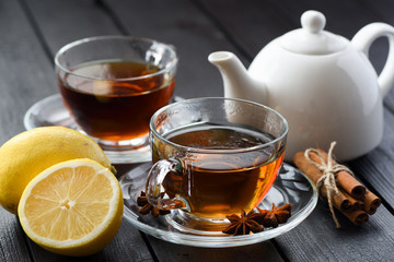 Hot healthy beverage. Black tea with lemon and spices on black background