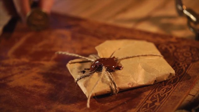 Shot of a vintage letter lying on the wooden table in a studio. Man is pushing stamper into wax paddle.