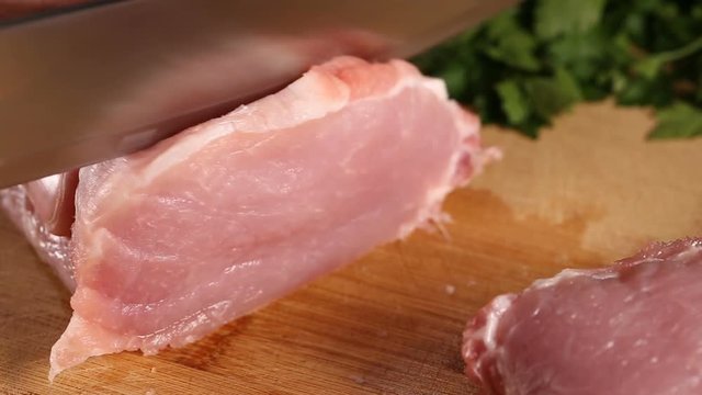Slicing raw pork meat on wooden cutting board