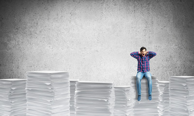 Attractive man sitting on pile of paper documents.