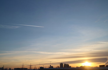 Cirrus clouds in the autumn sky in the evening at sunset, trail from the plane, evening over the industrial zone