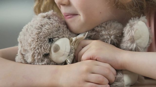 Lonesome child with teddy bear waiting for parents to take her from orphanage