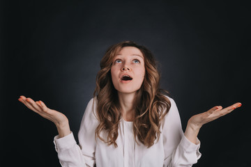 young attractive woman looking up arms outstretched, mouth open, waiting. On a dark background.