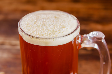 Close up of glass of beer with foam on a wooden table in a dark pub