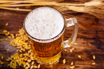 Above view of a glass of light beer with foam, with a wheat branch and wheat on a wooden table in a blurred background