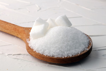 Cubes of sugar and granulated sugar with wooden spoon.