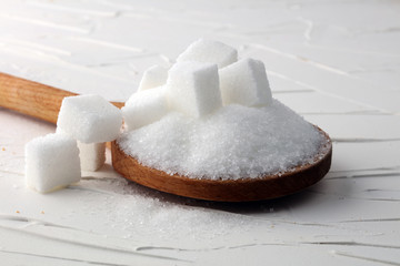 Cubes of sugar and granulated sugar with wooden spoon.