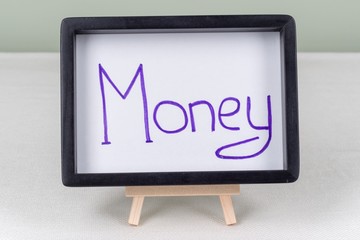 Text word money, in black frame, on white table.