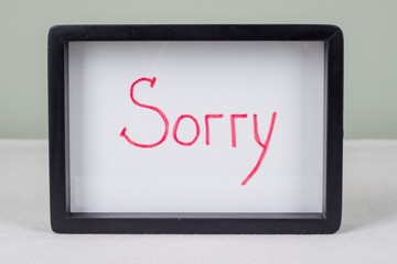 Text word SORRY, in black frame, on white table.