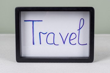 Text word TRAVEL, in black frame, on white table.