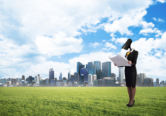 Camera headed woman standing on green grass against modern cityscape