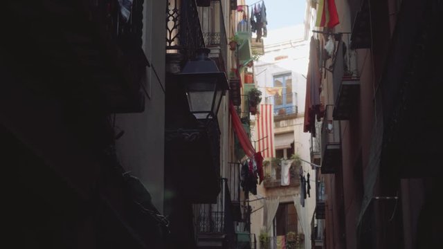 View of narrow street with balconies and windows with catalonian flag and laundry hanging on cords