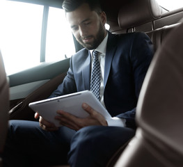 businessman with a digital tablet sitting in the back seat of a car