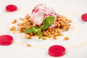 Scoop of ice-cream on roasted nuts decorated with mint and raspberry jelly