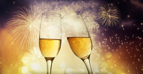 two champagne glasses ready to bring in the New Year - holiday lights and fireworks in the background