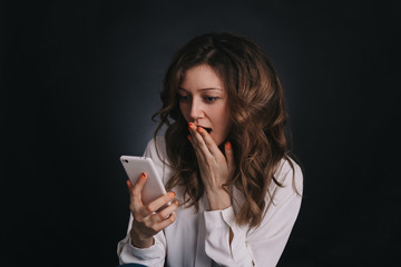 Young girl stares at the screen of your smartphone, read shocking news. Closeup on dark background.