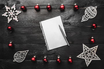 Upper, top, view from above, of wooden winter figurines, red toys notepad and pen on black background, with space for text writing, greeting.