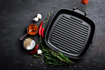 Empty cast-iron grill pan with ingredients for cooking on black background, top view