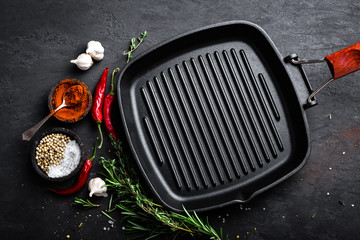 Empty cast-iron grill pan with ingredients for cooking on black background, top view - obrazy, fototapety, plakaty