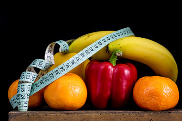 Tasty fruits and vegetables on an old dark wooden kitchen table. Banana, peppers and mandarins on the kitchen table along with the measure.