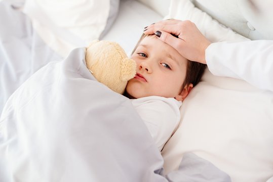 Doctor Examines Child Fever With Hand On Forehead.