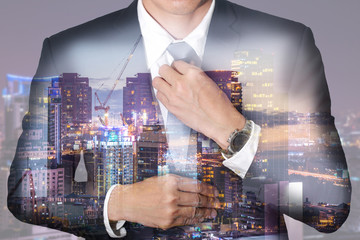 Double exposure of businessman held necktie dress to look good, construction crane and building and night cityscape as get ready of business and industrail concept