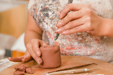 Close up of woman ceramist hands working with a tool over a sculpture on wooden table in workshop