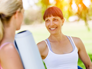 Fototapeta premium Two young women with a gym mat chatting in the park