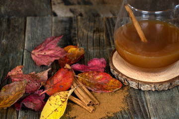 hot apple cider with cinnamon sticks and colorful autumn leaves on rustic wood