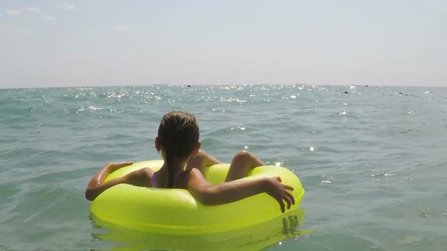 The child swims on the inflatable circle. A little girl enjoys the sea view.