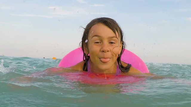A happy child is swimming in the sea. Little girl shows tongue in water.