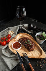 beautiful serving of meat steak on a wooden plate with salad, tomato sauce and a glass of red wine on a wooden dark background